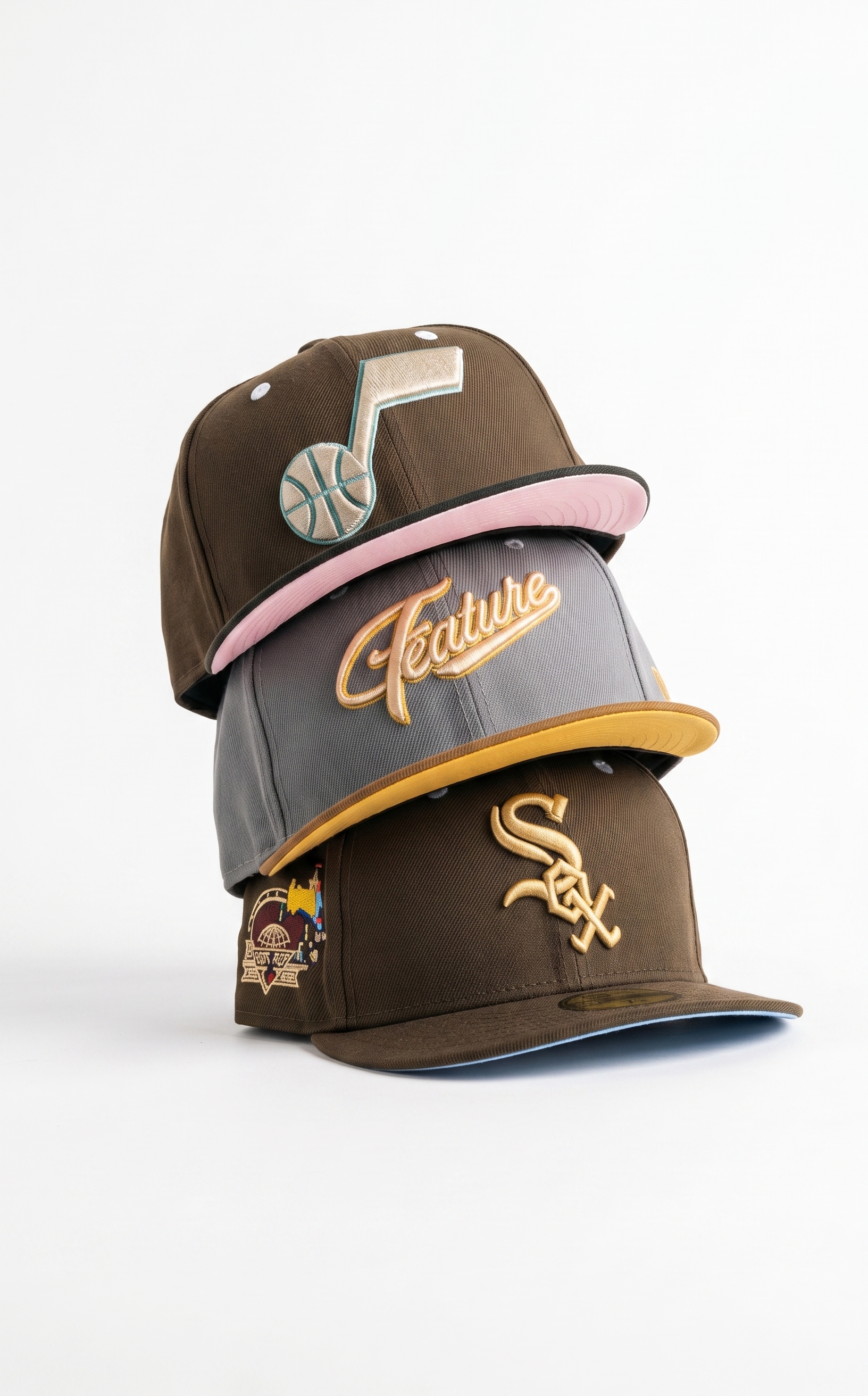 A stack of three premium fitted hats featuring a brown Utah Jazz cap, a grey Feature script cap, and a brown Chicago White Sox cap with a side patch.
