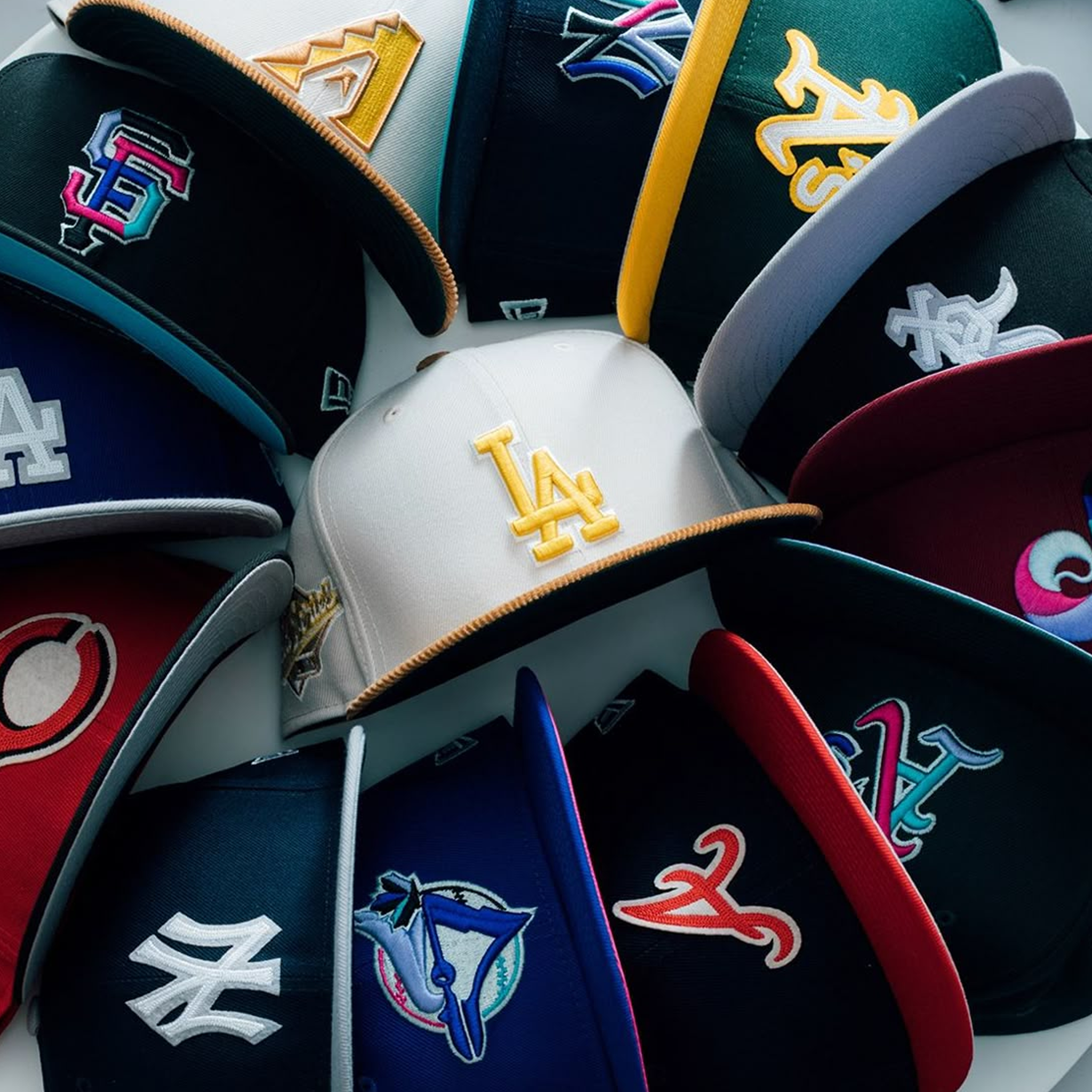 A circular arrangement of colorful MLB baseball caps, featuring a light grey LA Dodgers hat in the center.