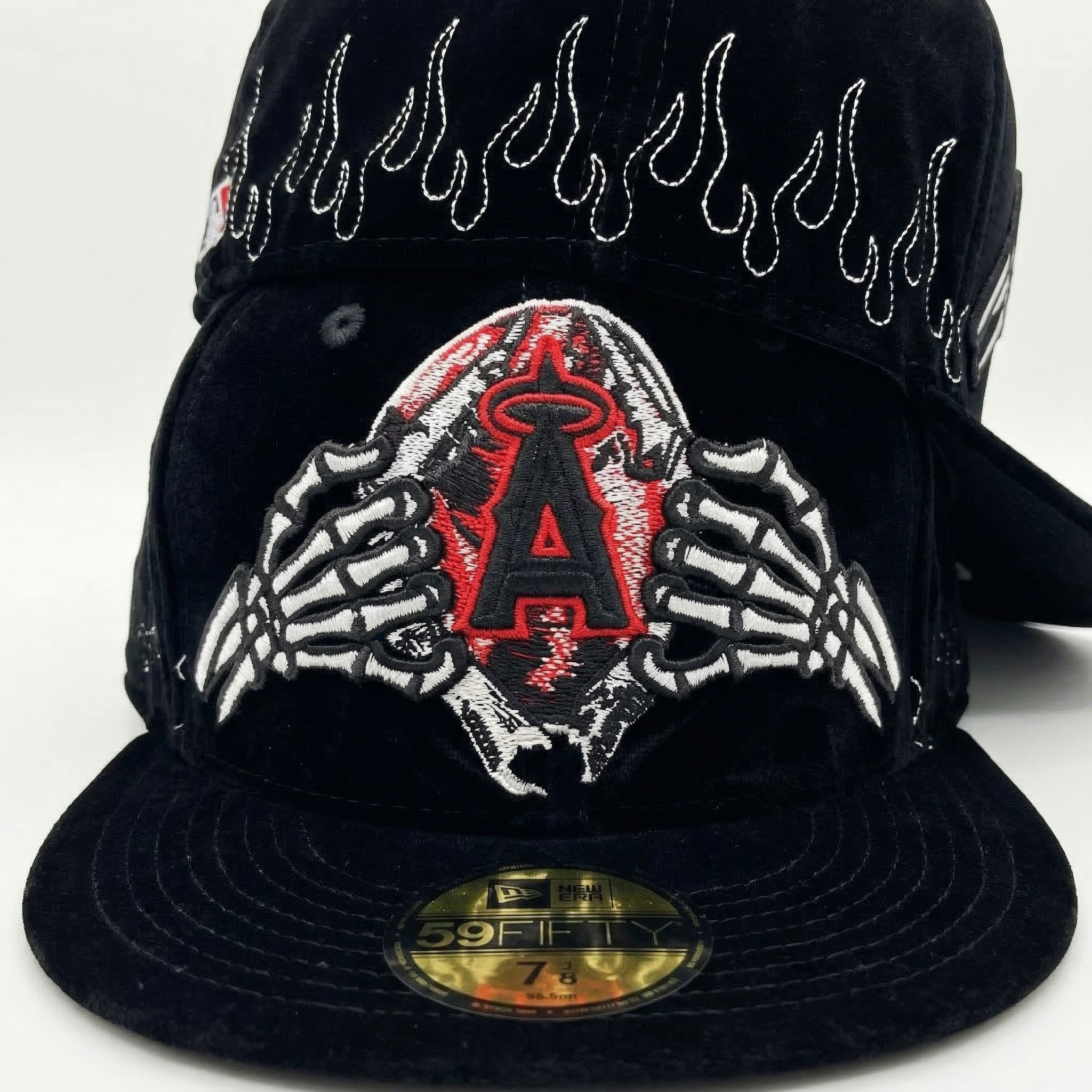 Close-up front view of a black velvet New Era flat-brim cap, showcasing the detailed texture of the velvet material and the detailed skeleton hand holding the red embroidered A-shield. The rear panel is resting behind, revealing additional intricate white flame embroidery.