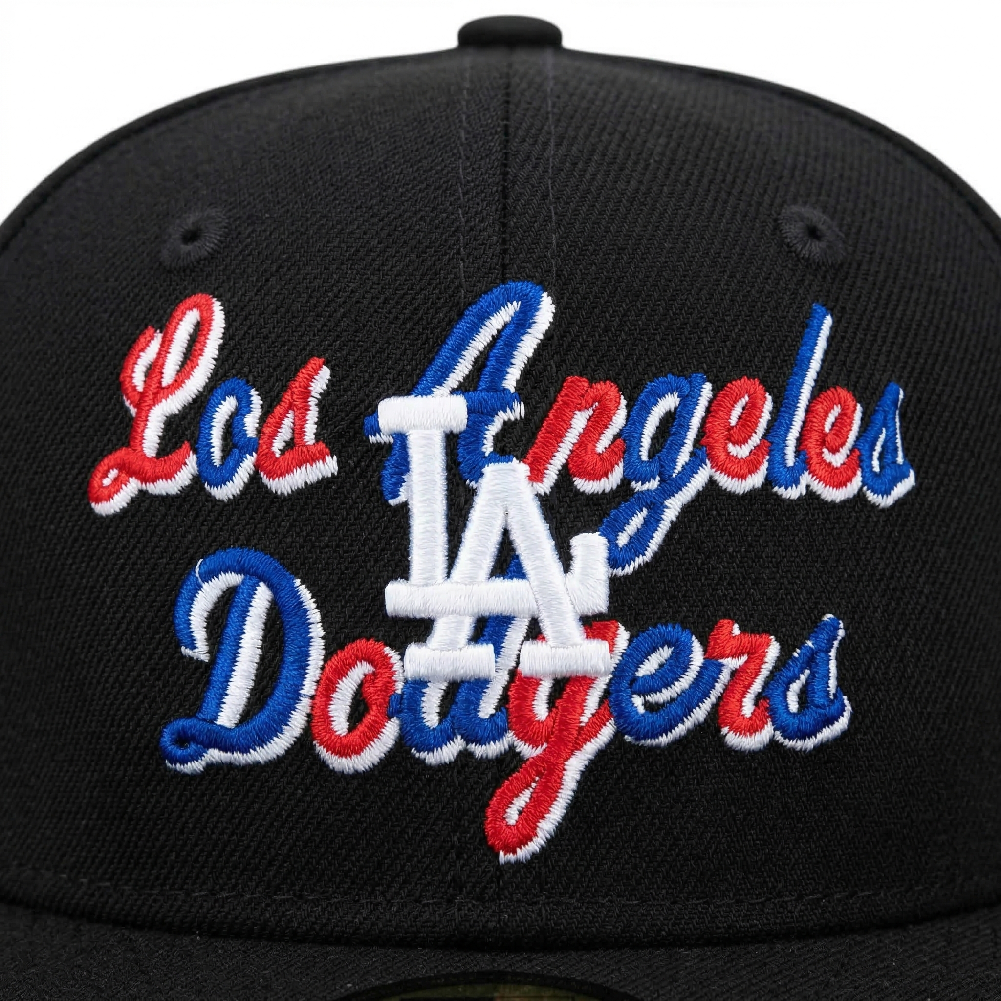 Front view close-up of a black LA Dodgers baseball cap, detailing the white interlocking LA logo surrounded by red and blue cursive embroidery.